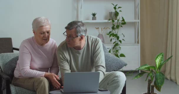 Šťastný starý běloch středního věku starý pár pomocí notebooku technologie spolu mluví dělat on-line nakupování vybrat produkt čtení diskutovat o internetových novinkách objednávání vstupenek na webových stránkách doma — Stock video