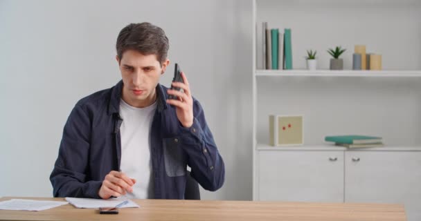 Tired man overworked male freelance businessman entrepreneur sits at table in home office calling dials phone number on calculator by mistake speaks on mobile device answers call, exhaustion concept — Stock Video