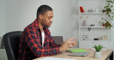 Afro iş adamı programcısı ofisinde oturuyor eline bir şişe antiseptik damlalar alıyor antibakteriyel jel tedavisi avuç içlerini virüsten koruyor enfeksiyondan korunuyor laptopta işe yarıyor