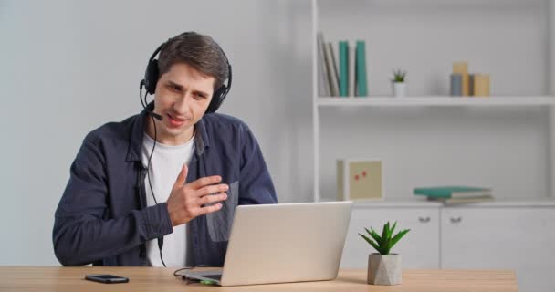 Homem de negócios em camisa casual senta-se à mesa faz chamada de vídeo bate-papo usa fones de ouvido microfone principal fala em câmera web laptop sente dúvida negocia falando on-line mostra polegares para cima, conversa remota — Vídeo de Stock