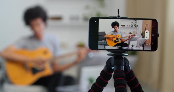 Visualizzazione dallo schermo del telefono cellulare giovane insegnante di musica afroamericana tutor registrazione video a casa a suonare la chitarra conduce lezione online utilizzando smartphone canta canzone impegnata nel suo hobby preferito — Video Stock