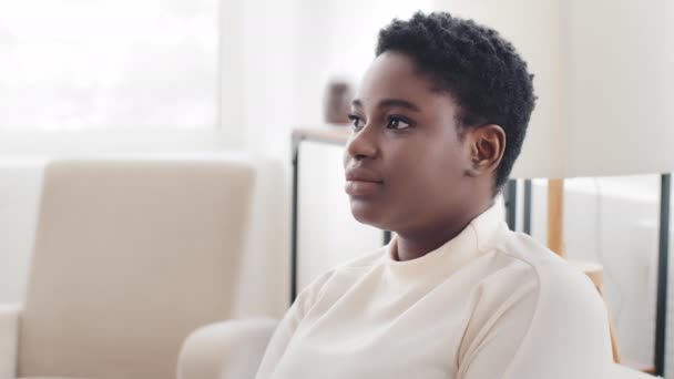 Portrait afro american girl ethnic model with short hair looking to side sitting in profile at home turns head looks at camera smiling toothy, close-up happy african mixed race woman posing indoors — Stock Video