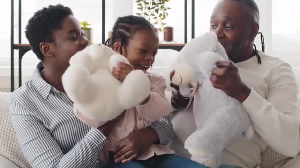 Χαρούμενη οικογένεια Αφρο-Αμερικανών τριών γενεών στο σπίτι να παίζει με αρκουδάκια σε κοντινό πλάνο πορτραίτο. Μικρή μαύρη κόρη εγγονή έχοντας διασκέδαση με την ενήλικη μητέρα και ο παππούς δίνει πέντε με το χέρι — Αρχείο Βίντεο