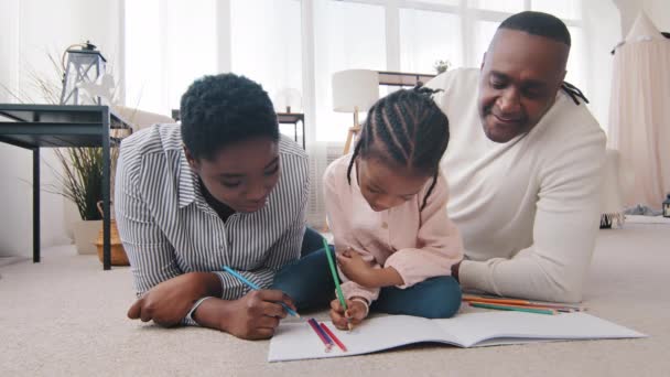 アフリカ系アメリカ人の両親3世代の祖父、母、娘の孫娘が床に自宅で描画します。大人お母さん中年女性成熟しましたアフリカ人男性お父さん助けて女の子とともに宿題 — ストック動画