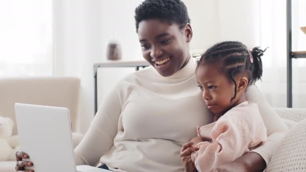 Retrato africano afro-americano preto étnico mãe sentado no sofá em casa interior com bonito filhinho bebê criança acenando adeus olhando para laptop online vídeo chat conferência assistindo filme — Vídeo de Stock