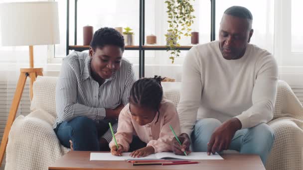 Afro amerikansk familj tre generationer vuxen mor kvinna äldre syster med liten flicka dotter skolflicka barnbarn elev och mogen farfar man ritar hem skolhjälp med läxor — Stockvideo
