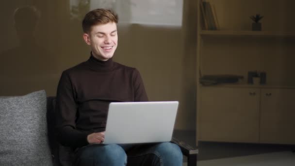 Щасливий молодий чоловік робить онлайн-дзвінок, використовуючи ноутбук і сучасний комп'ютерний додаток вдома для віддаленої розмови. Юнак з Кавказу сміється, розмовляючи з друзями на відео-конференції. — стокове відео