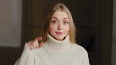 Sarışın model, kafası karışmış, kafası karışmış, küçük şekiller gösteren, parmaklarıyla küçük boy jestler yapan, omuz silken, evde poz veren bir kadın.