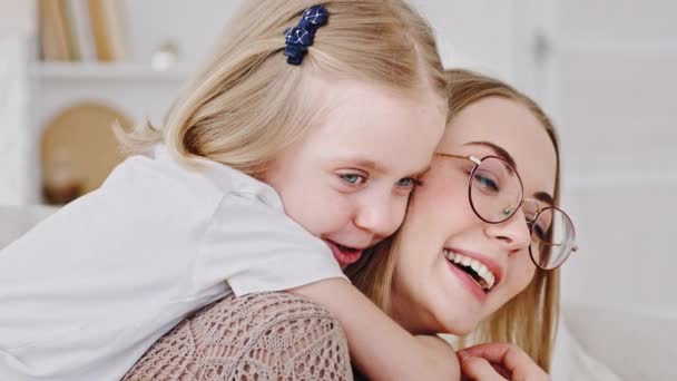 Family home portrait little daughter blonde cute child hugs mom young woman with glasses around neck cuddles beloved parent, close-up happy mother laughs smiling talking with baby girl relaxing indoor — Stock Video