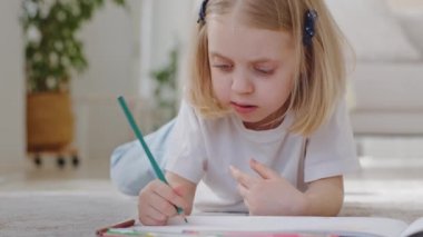 Küçük tatlı kız çocuğu anaokulu çocuğu sarışın liseli kız evde yerde yatan kalemlerle yaratıcı resimler çiziyor, bebek hobilerine odaklanıyor, boş zamanlarında boş zamanlarında.