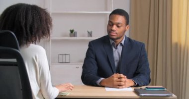 Beyaz gömlekli, tanınmayan kıvırcık saçlı kadın masada oturuyor ve genç iş adamı Afro-Amerikan profesyonel ofis çalışanına dolar maaşı veriyor.