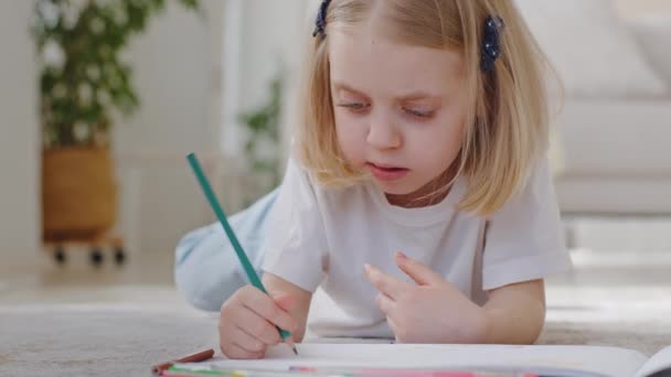 Liten söt flicka dotter barn förskola småbarn barn blond skolflicka ritar kreativ bild med pennor på papper liggande på golvet hemma, baby koncentrera sig på hobbies läxor, fritid — Stockvideo