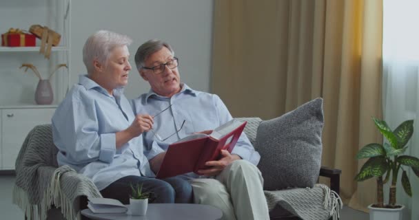 Två gamla människor äldre par saknade man och hustru sitter på soffan i mysiga vardagsrum minns trevliga stunder från tidigare titta på bilder av sina älskade barn, vända sidor fotoalbum — Stockvideo