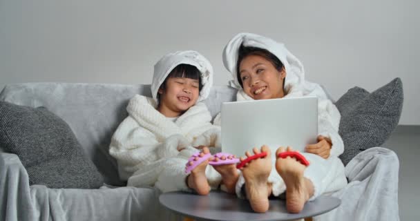 Asyalı ailenin şefkatli annesi ve kızı kanepede oturuyor. Akşam hijyen prosedürleri yapıyor. Pedikür, duştan sonra bornoz ve havlu giyiyor. — Stok video