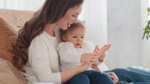 Caucasian young mother with baby little girl talking hugs spends time together at home, loving mom woman babysitter cuddling kid toddler infant newborn child tickles, motherhood love and childhood — Stock Video