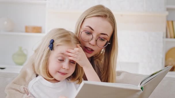 Portrait caucasian mother in glasses reads book fairy tale to child little daughter teaches baby at home, close-up reading story mom spends time with kid, concept of preschool education and childcare — Stock Video