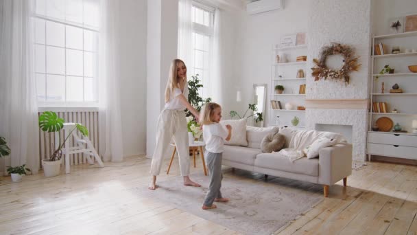 Jovem mãe loira mãe dançando com a filha pequena menina em casa sala de estar interior, mãe alegre e criança ativa criança família desfrutar de dança se divertir movendo-se para a música juntos no fim de semana interior — Vídeo de Stock