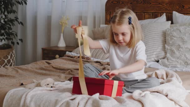 Malá kavkazské dítě dcera blondýnka dítě narozeniny dívka sedí na posteli v útulné ložnici otevře velký červený dárkový box se žlutou stuhou rozbaluje dárky cítí smutné zklamání frustrace z prázdného kufříku — Stock video