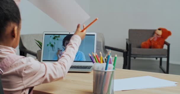 Pequeña colegiala étnica que estudia en casa dibuja hablar con el profesor en videollamada en línea utiliza portátil escoge lápiz escucha a los tutores consejos dibuja imagen, aprendizaje remoto durante cuarentena de bloqueo — Vídeo de stock