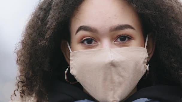 Gyönyörű sötét bőrű fekete fiatal nő afro frizurával visel védő maszkot COVID vírus, afro-amerikai lány orvosi légzőkészülék áll a szabadban a nyilvános térben, zárlat koncepció — Stock videók