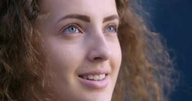 Sokakta poz veren kafadan vurmalı model kadın. Yakın plan, gülümseyen bir kadın. Uzağa bakıyor, mavi gözlü. Mükemmel ciltli, kıvırcık, genç kız portresi. Sağlıklı beyaz dişler..