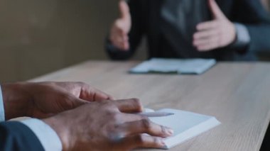 Kapalı erkek elleri deftere notlar yazar, çok ırklı iki meslektaşın ofis masasında evrak kağıtlarıyla oturup, strateji hakkında beyin fırtınası yapar.