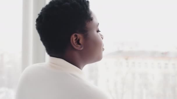 Voltar ver Africano americano menina millennial étnico preto misto mulher afro dona de casa com cabelo curto olhando para fora janela contemplando sonhando pensar sobre planos se transforma olhando para câmera sorrindo — Vídeo de Stock