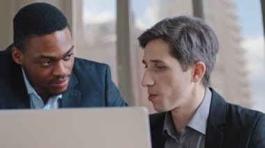 İki kendine güvenen Afrikalı erkek ve Kafkasyalı iş adamı online hizmet uygulamasında verileri gözden geçiriyorlar, bilgisayarlı ekran tartışması projesine bakıyorlar.