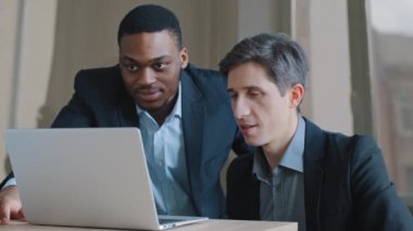 Ofisteki iki dalgın erkek arkadaş bilgisayar uygulaması kullanarak dizüstü bilgisayara bakan internet sunucusuyla ilgili sorunları tartışıyor, beyaz yönetici ağdaki Afro-Amerikalı iş adamına veri gösteriyor.