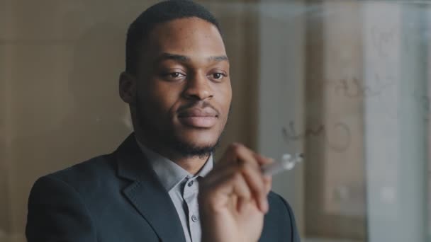Portrét zaostřeného afro amerického podnikatele 30s výkonný manažer píše vzorce finanční výpočty spoléhat na transparentní skleněnou tabuli, analyzuje start-up, dělá inovace, dostane úspěch výsledek — Stock video