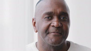 Erkek insan portresi afro amerikan yetişkin olgun orta yaşlı yaşlı adam evde, yakın plan 50 'li yaşlarda esmer tenli buruşuk Afrikalı bir adam kameraya bakıyor sakin bir ifadeyle evde yalnız poz veriyor