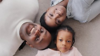 Üst tabaka Afro-Amerikan ailesi yerde yatan yetişkin etnik anne kadın, karışık ırk baba baba koca ve küçük afro siyah çocuk kameraya bakıp gülümsüyor.