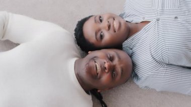 Afro-Amerikan çifti orta yaşlı zenci koca ve etnik eşin yerde birlikte yatıp kameraya bakarken içtenlikle gülümsemesi, Afrikalı olgun erkek ve genç kadının mutlu yüzlerini kapatması.