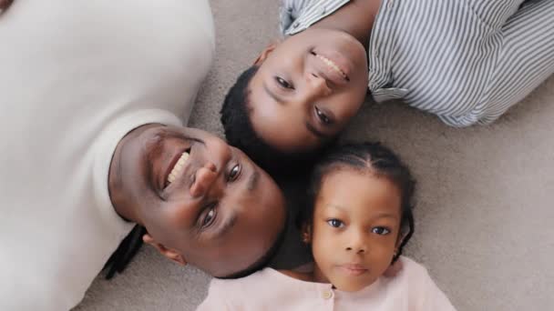 Top view portræt afrikansk amerikansk familie liggende på gulvet voksen etnisk mor kone kvinde, blandet race moden midaldrende mand far mand bedstefar og lidt afro sort pige barn kigger på kamera smilende – Stock-video