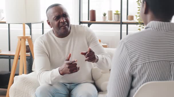 Oudere Afrikaanse man van middelbare leeftijd vader patiënt zittend op de bank binnen stelt vraag praten met onherkenbare afro vrouw zwarte dame psycholoog dochter communiceren gesprek overleg — Stockvideo