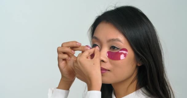 Close-up beautiful young asian ethnic woman korean teen girl applying moisturizing patches on under eyes area, feeling satisfied joy with domestic spa skincare treatment make-up morning procedures — Stock Video