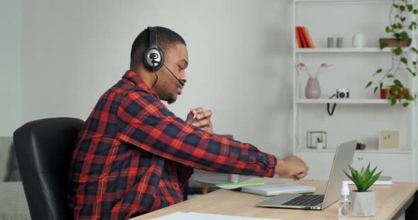 Yan görüşlü Afrikalı öğrenci kablosuz kulaklıkla bilgi yazıyor e-öğrenme dili ile, işadamı wathing webinar profesyonel becerileri geliştiriyor video uygulaması laptopunu kullan — Stok video