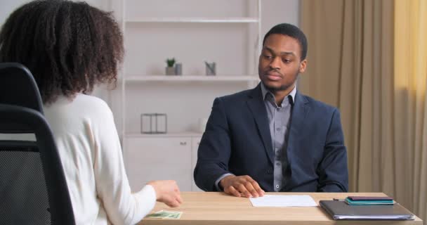 Unrecognizable businesswoman grateful client with curly hair in white shirt sits at office table talking to man partner lawyer seller gives money for services afro american businessman receives salary — Stock Video