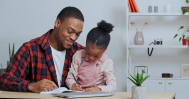 Afro-Amerikan babası küçük kızına mektup yazmayı öğretiyor. Not defterine not alıyor. Çocuk evde öğreniyor.