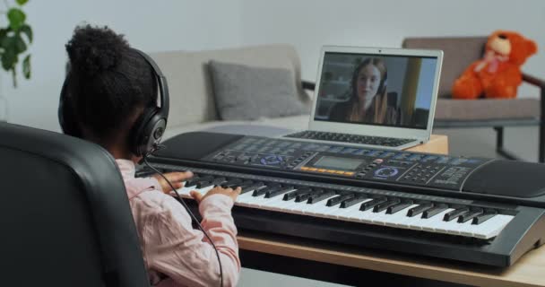 Felismerhetetlen kislány afro amerikai gyerek visel fejhallgatót teszi video hívás női tanár kommunikál online oktató tanulni játszani elektronikus zongora szintetizátor, tanulás zárlat alatt