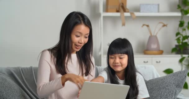 Asian family young mother and cute schoolgirl child sitting on couch making video call to their beloved father waving hands in greeting saying hello looking at laptops webcam communicating remotely — Stock Video