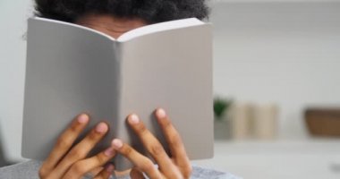 Genç afro-amerikalı çocuk yüzünü kitapların arkasına sakladı kitap okudu ders kitapları şok edici duyguları ifade etti beklenmedik komplolar kurdu