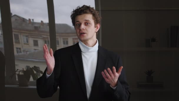 Молодой взрослый кавказский бизнесмен-профессионал успешный парень предприниматель сотрудник носит черный официальный костюм стоит в одиночестве в офисе разговаривая, глядя в камеру жестом показывая большие пальцы вверх — стоковое видео