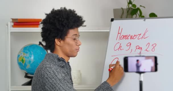 Göndör hajú fiatal afro-amerikai férfi oktató visel szemüveg áll a táblán írni tárgyalások magyarázza lecke osztály vezet előadások videó mobiltelefon, elektronikus oktatás karantén alatt — Stock videók