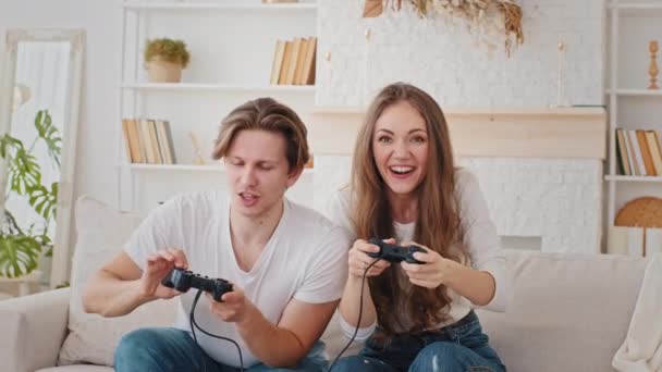 Vrolijke paar millennials Kaukasische getrouwde man en vrouw spelen videogame samen thuis lachen plezier genieten wedstrijd wedstrijd spelen console spel, man klikt op controller meisje voorkomt winnen — Stockvideo