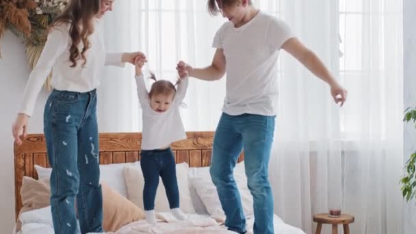 年轻可爱的白种人父母在家里玩耍，享受着与小女儿躺在床上玩耍的快乐时光，父母们手拉着小女儿在空中玩耍 — 图库视频影像