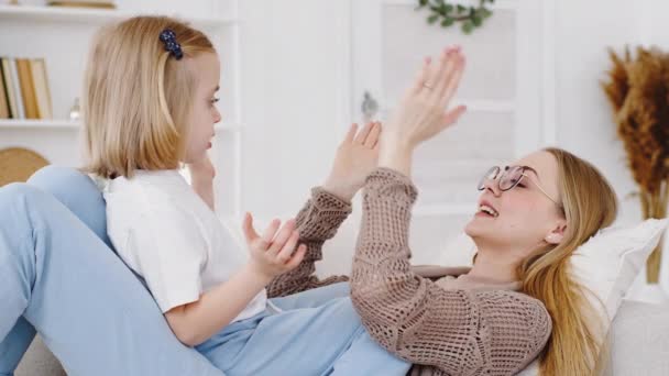 Portret vrolijke moeder oudere zus babysitter ligt op de bank thuis spelen patty taart spel met kleine meisje dochter glimlachen, close-up familie weekend mam en kind klappen handen geven vijf met palmen — Stockvideo