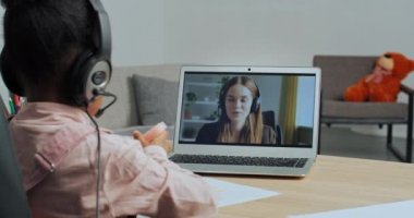 Afrikalı Amerikalı liseli kızın internetteki öğretmen kadınla resim yapmayı öğrenmesi, kulaklık takması, ev masasında oturması, video konferansı yoluyla öğretmenle konuşması, e-öğrenme,