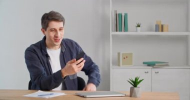 Genç, mutlu, serbest çalışan bir iş adamı masada oturmuş gündelik tişörtler giyiyor ve akıllı telefonuyla video görüşmesi yapıyor. 30 'lu yaşlarda neşeli bir adam elinde cep telefonuyla arkadaşlarıyla online konferansta konuşuyor.
