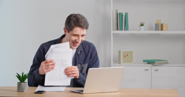 Feliz caucásico millennial hombre de negocios satisfecho hombre ganador haciendo video llamada en línea chat sentado en casa oficina hablando en el ordenador portátil webcam mostrando documento buen aviso bancario contrato exitoso — Vídeos de Stock